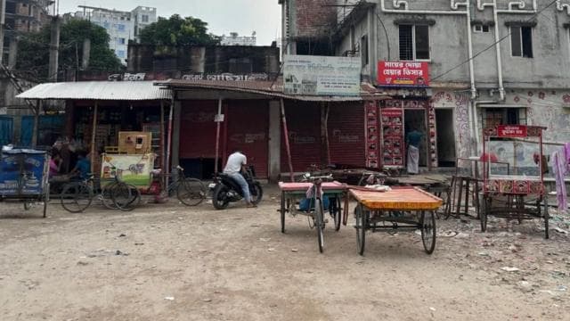 একটি দোকানের শাটার নামানো, সামনে দুটি ভ্যান। পাশে একজন মোটরসাইকেল চালক বসে আছেন