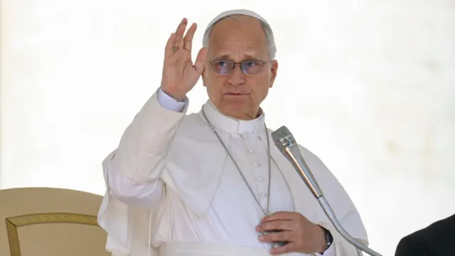 সাদা পোপীয় পোশাক পরিহিত পোপ লিও একটি মাইক্রোফোনে কথা বলছেন