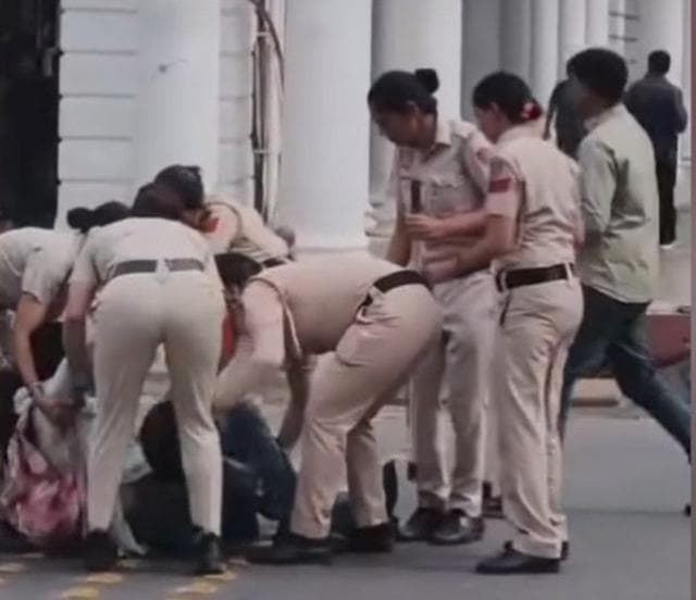 রাস্তায় পড়ে আছেন শরণ্যা শর্মা এবং তাকে নিয়ে যাওয়ার চেষ্টা করছেন নারী পুলিশকর্মীরা