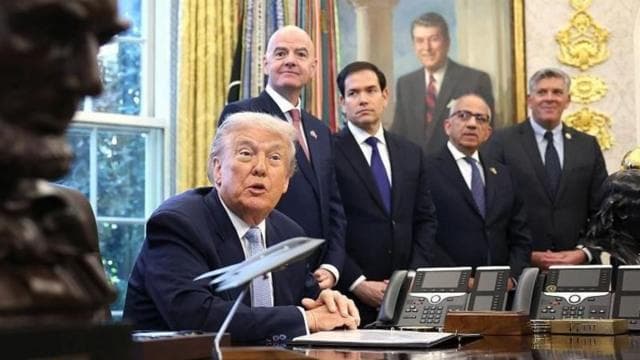 ডোনাল্ড ট্রাম্প বসে আছেন। পেছনে ইনফান্তিনোসহ আরো কয়েকজন দাঁড়ানো।